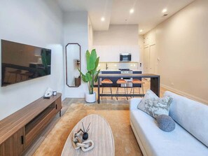A modern living room with a flat-screen TV, a wooden coffee table, a light blue sofa, and a dining area with a kitchen in the background. - The Avery – Boutique Bucktown/WP Studio by Transit (Chicago)