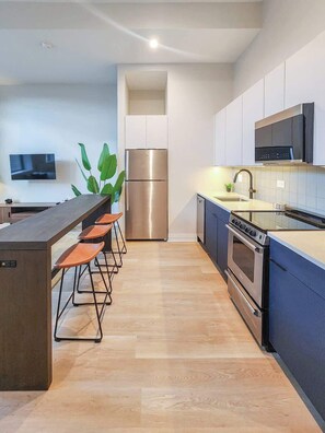 A modern kitchen with a central island, stainless steel appliances, and a flat-screen TV. - The Avery – Boutique Bucktown/WP Studio by Transit (Chicago)
