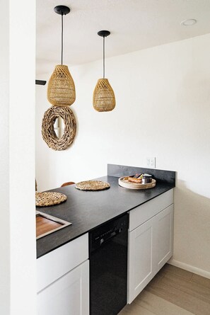 A kitchen with a black countertop, white cabinets, and a black dishwasher. There are woven baskets on the counter and two hanging pendant lights. - Modern and Relaxing Sedona Oasis - Bedouinn (Sedona)