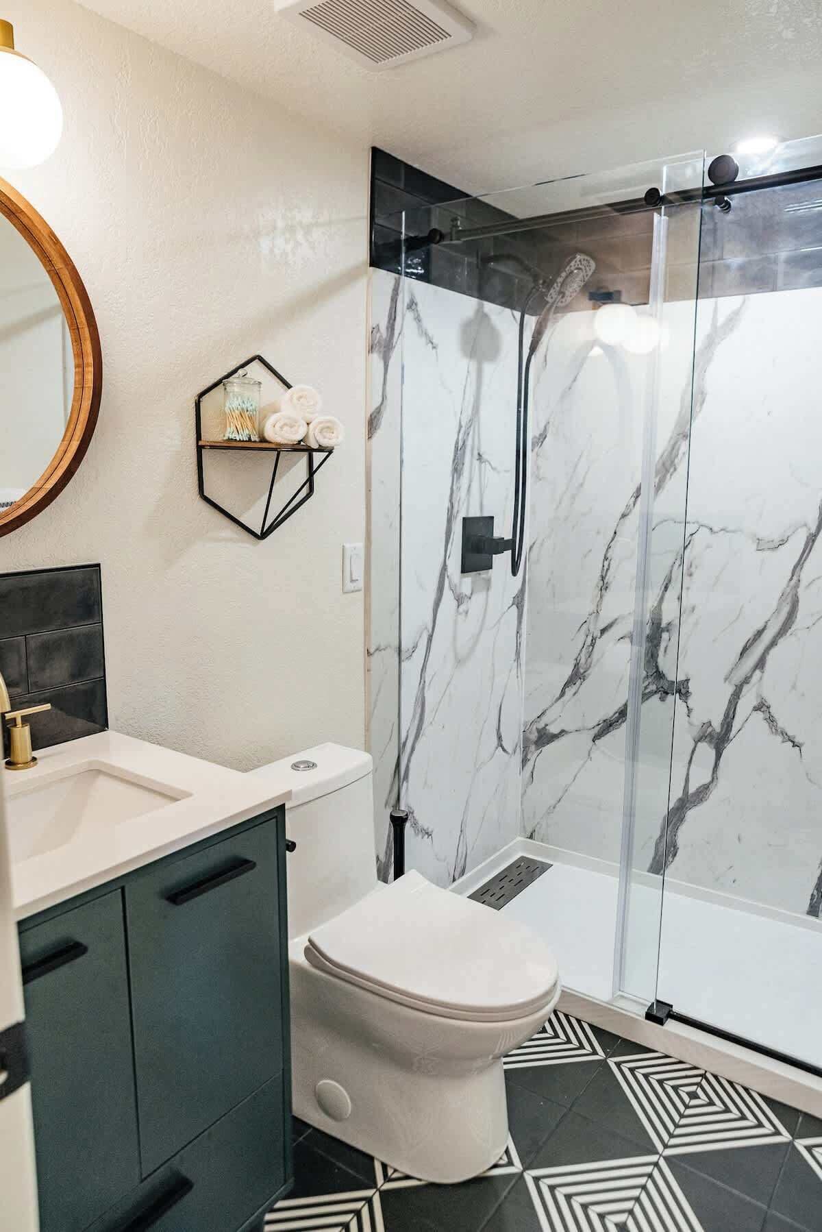 Een moderne badkamer met een douche in marmer, toilet, wastafel en spiegel.