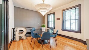 A dining area with a round table, blue chairs, a large 'R' decoration, a hanging light fixture, and windows with blinds. - Feelin’ Nauti Near Wrigley (Chicago)