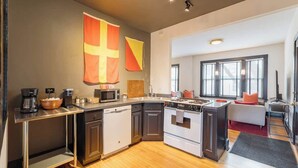 A modern kitchen with a central island, a dishwasher, a stove, and a microwave. There are large windows providing natural light. - Feelin’ Nauti Near Wrigley (Chicago)