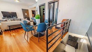 A modern living room with a flat-screen TV, a sofa, and blue chairs. A staircase with a metal railing leads to another room. - Feelin’ Nauti Near Wrigley (Chicago)