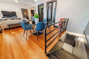 Ein modernes Wohnzimmer mit einem Flachbildfernseher, einer Couch und blauen Sesseln. Eine Treppe mit Metallgeländer führt zu einem weiteren Raum.