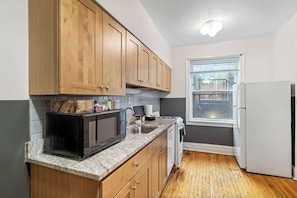 A compact kitchen with wooden cabinets, a microwave, a sink, and a window. - Toad Hall near Wrigley (Chicago)