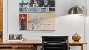 Un moderno spazio ufficio con una scrivania, una sedia da ufficio nera e opere d'arte alle pareti.