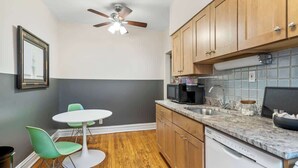 Una cucina funzionale con mobili in legno, un forno a microonde, una macchina da caffè e un'lavastoviglie. C'è un piccolo tavolo da pranzo con due sedie.