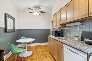 A compact kitchen with wooden cabinets, a microwave, a coffee maker, and a dishwasher. There is a small dining table with two chairs. - Toad Hall near Wrigley (Chicago)