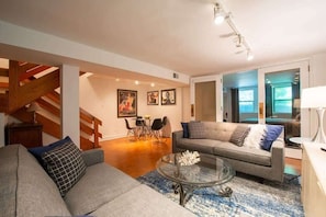 A modern living room with a grey sofa, a glass coffee table, and a staircase. - One-of-a-Kind Apartment In Old Town! (Chicago)