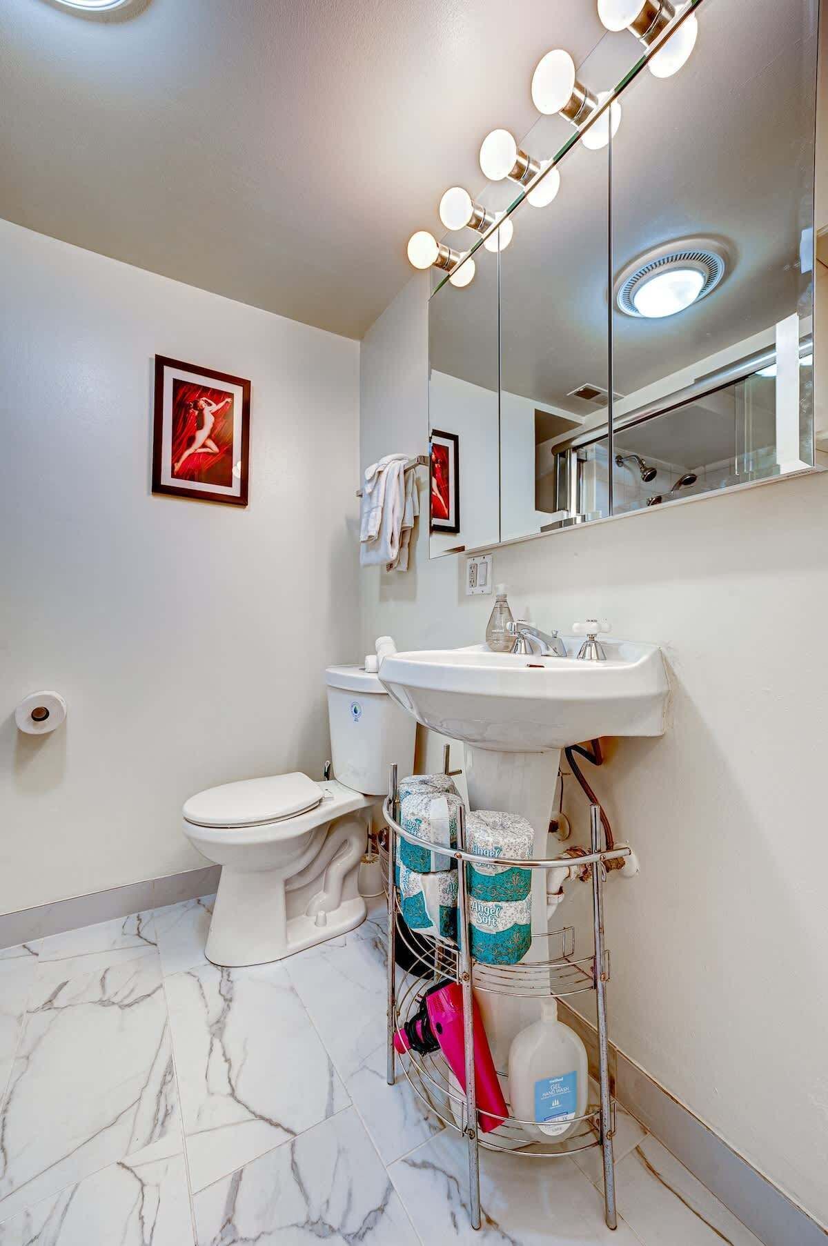 A bathroom with a toilet, sink, mirror, and marble floor.