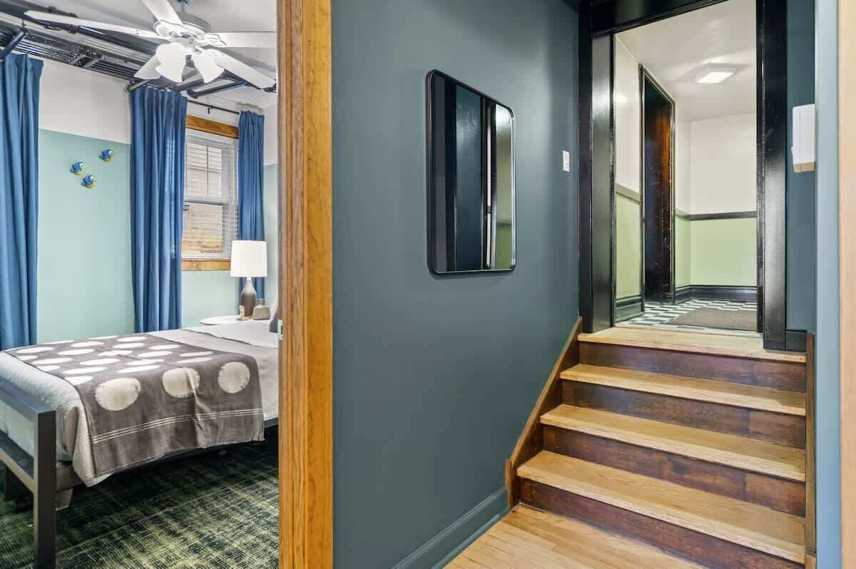 Une chambre d’hôtel comprenant un lit, un bureau, une chaise, une fenêtre avec des rideaux, un ventilateur de plafond et un escalier.