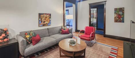 A living room with a grey sofa, red armchair, round coffee table, and a TV stand.