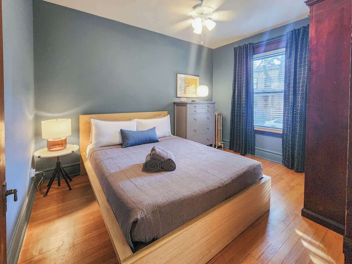 A neatly made bed with a grey blanket, a bedside lamp, and a small table with a lamp.