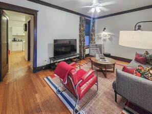 Ein modernes Wohnzimmer mit einem Flachbildfernseher, roten und grauen Sofas, einem Couchtisch und einem Deckenventilator.