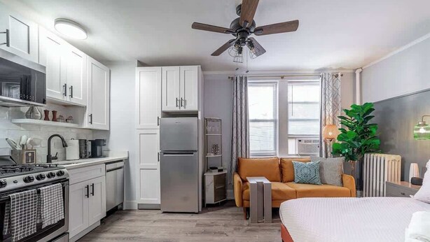 A compact living space with a kitchenette, a bed, a sofa, and a ceiling fan. - Studio Beau - Steps from Lincoln Park Zoo & Lake (Chicago)