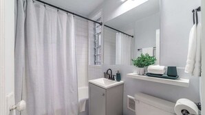 A modern bathroom with a shower curtain, a sink, a mirror, and a toilet. - Studio Beau - Steps from Lincoln Park Zoo & Lake (Chicago)