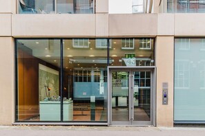 Ein moderner Gebäudeeingang mit großen Glasüren, einem digitalen Zahlenschloss und einem Schild mit der Aufschrift 'Dance Square Apartments 45 to 27'.