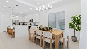 Een moderne keuken met witte kasten, een centraal eiland en een eethoek met houten stoelen.