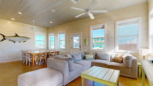 A spacious living room with a large gray sectional sofa, a wooden coffee table, and a dining area with wicker chairs. - GV628, Shared Pool, Pet Friendly, Charcoal Grill, Close to Beach (Port Aransas)