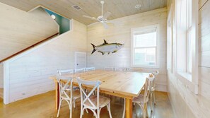 A wooden interior with a dining table, chairs, a ceiling fan, and a fish wall art piece. - GV628, Shared Pool, Pet Friendly, Charcoal Grill, Close to Beach (Port Aransas)