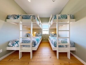A room with bunk beds, wooden flooring, and a window providing natural light. - GV628, Shared Pool, Pet Friendly, Charcoal Grill, Close to Beach (Port Aransas)