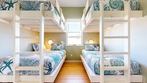A bunk bed room with two beds, each with a starfish-patterned bedspread, and a small window at the end of the room. - GV628, Shared Pool, Pet Friendly, Charcoal Grill, Close to Beach (Port Aransas)