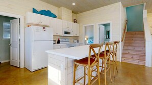 A kitchen with white cabinets, a refrigerator, a microwave, and a stove. There are wooden chairs with red cushions. - GV628, Shared Pool, Pet Friendly, Charcoal Grill, Close to Beach (Port Aransas)