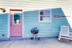 Ein Haus mit einer rosafarbenen Tür, einem Grill, einem weißen Plastikstuhl und einem an der Wand hängenden Baseballschläger.