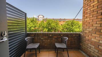 Un balcón con dos sillas, un muro de ladrillo y vista a un edificio con un reloj.