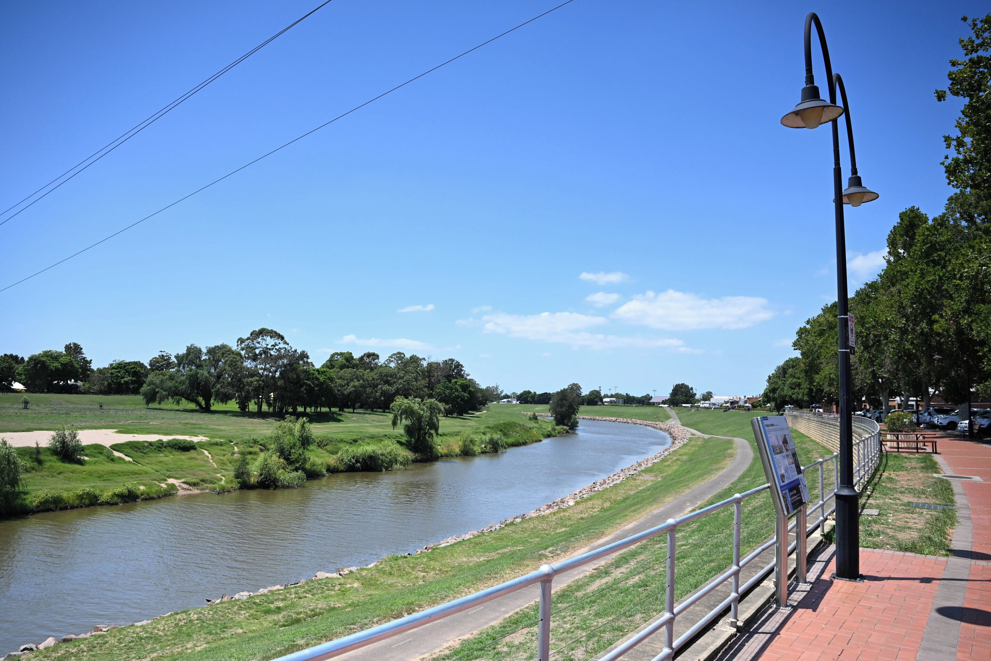 A riverside walkway with a metal railing, a street lamp, and a signboard.
