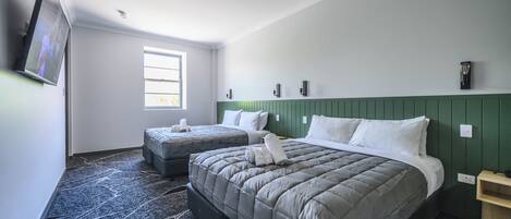 Habitación de hotel con dos camas, un televisor, una ventana y una pared verde.