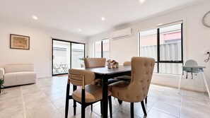 A dining area with a table, chairs, and a view of the outside. - Lyra Home by GoodLive (Beveridge)