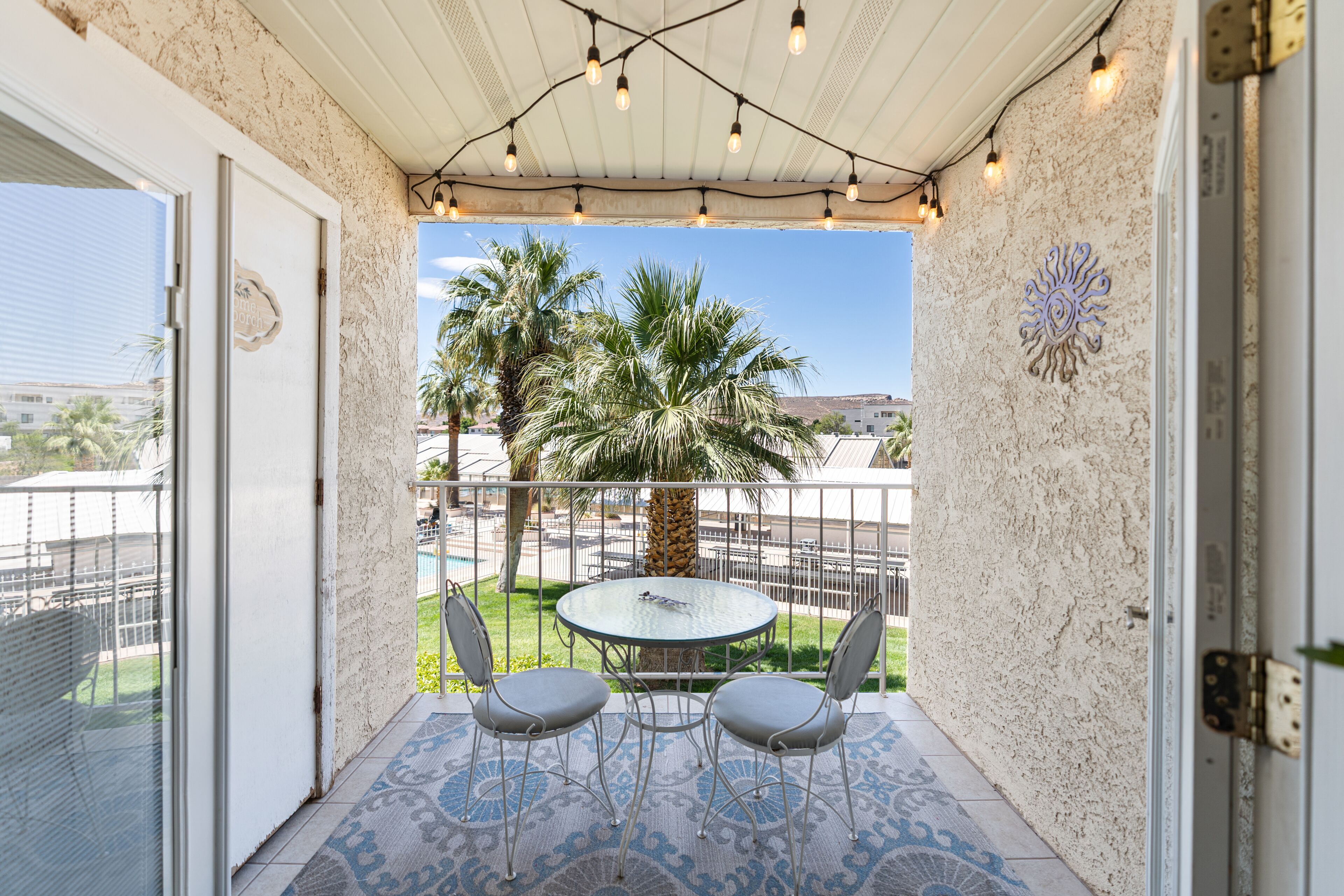 Une terrasse couverte avec une table et des chaises en verre, un sol à motifs et une vue sur les palmiers et les bâtiments.