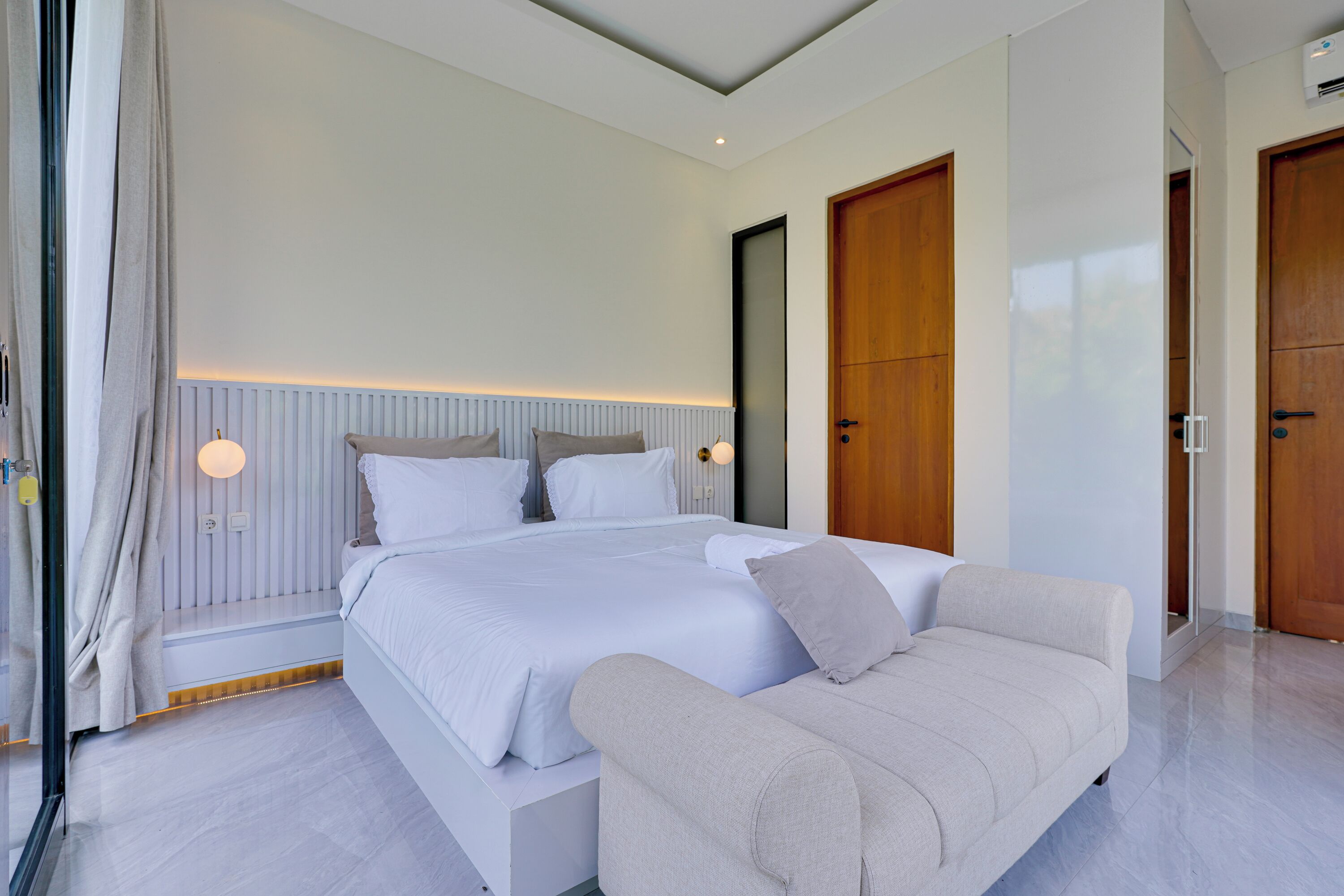 A modern bedroom with a large bed, a sofa, and two wooden doors.
