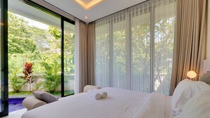 A large bed with white linens, a view of a lush garden through a glass door, and a modern room design. - Villa Ease - Nusa Dua (Nusa Dua)