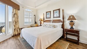 A spacious bedroom with a large bed, a wooden nightstand, two wall-mounted lamps, and a view of the outdoors through a window with curtains. - Experience oceanfront luxury at 32 Ocean Place, a cozy 2-bedroom condo in Fernandina Beach. (Fernandina Beach)