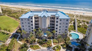 A multi-story hotel with a central courtyard, surrounded by palm trees and a swimming pool. - Experience oceanfront luxury at 32 Ocean Place, a cozy 2-bedroom condo in Fernandina Beach. (Fernandina Beach)