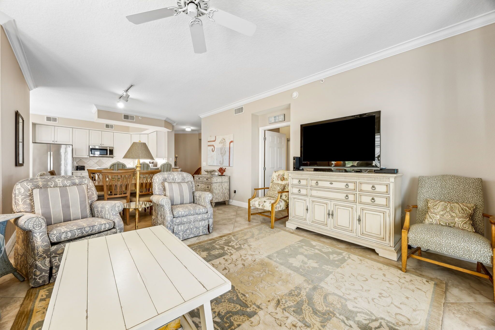 A spacious living room with a white coffee table, patterned sofas, a TV, and a dining area with a chandelier.