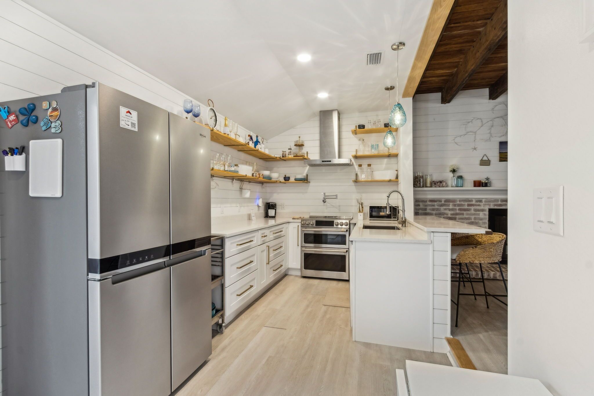 A modern kitchen with a stainless steel refrigerator, built-in oven, and wooden shelves.