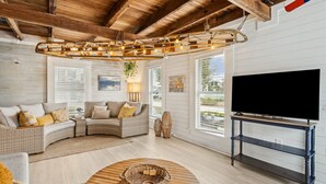 A cozy living room with a curved sofa, a TV on a stand, and a wooden ceiling. - Charming 3BR home in Fernandina Beach with wooded views and space for 8! (Fernandina Beach)