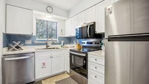 A modern kitchen with stainless steel appliances, white cabinetry, and a window with a view of greenery.