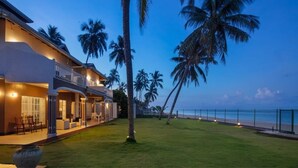 Una propiedad frente a la playa con una casa grande, un césped bien cuidado y varias palmeras.