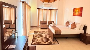 Una habitación de hotel con cama, escritorio, silla, ventilador de techo y un cuadro en la pared.