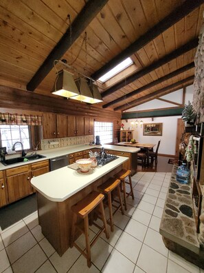 A rustic kitchen with wooden cabinets, a large island with stools, a stone fireplace, and a dining area with a table and chairs. - Beautiful 5 bedroom cabin on the Lake of the Hills.  (Eagle River)