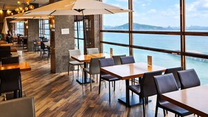 A modern restaurant with wooden flooring, large windows offering a view of the sea, and contemporary lighting fixtures. - SainTree Hotel (Incheon)