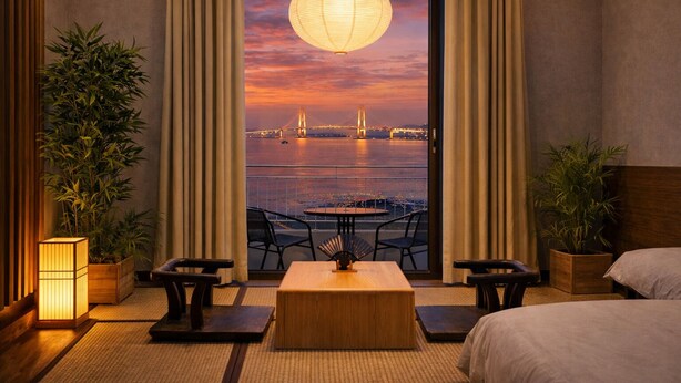 A hotel room with a view of a bridge at sunset, a dining table, chairs, a sofa, and two potted plants. - SainTree Hotel (Incheon)
