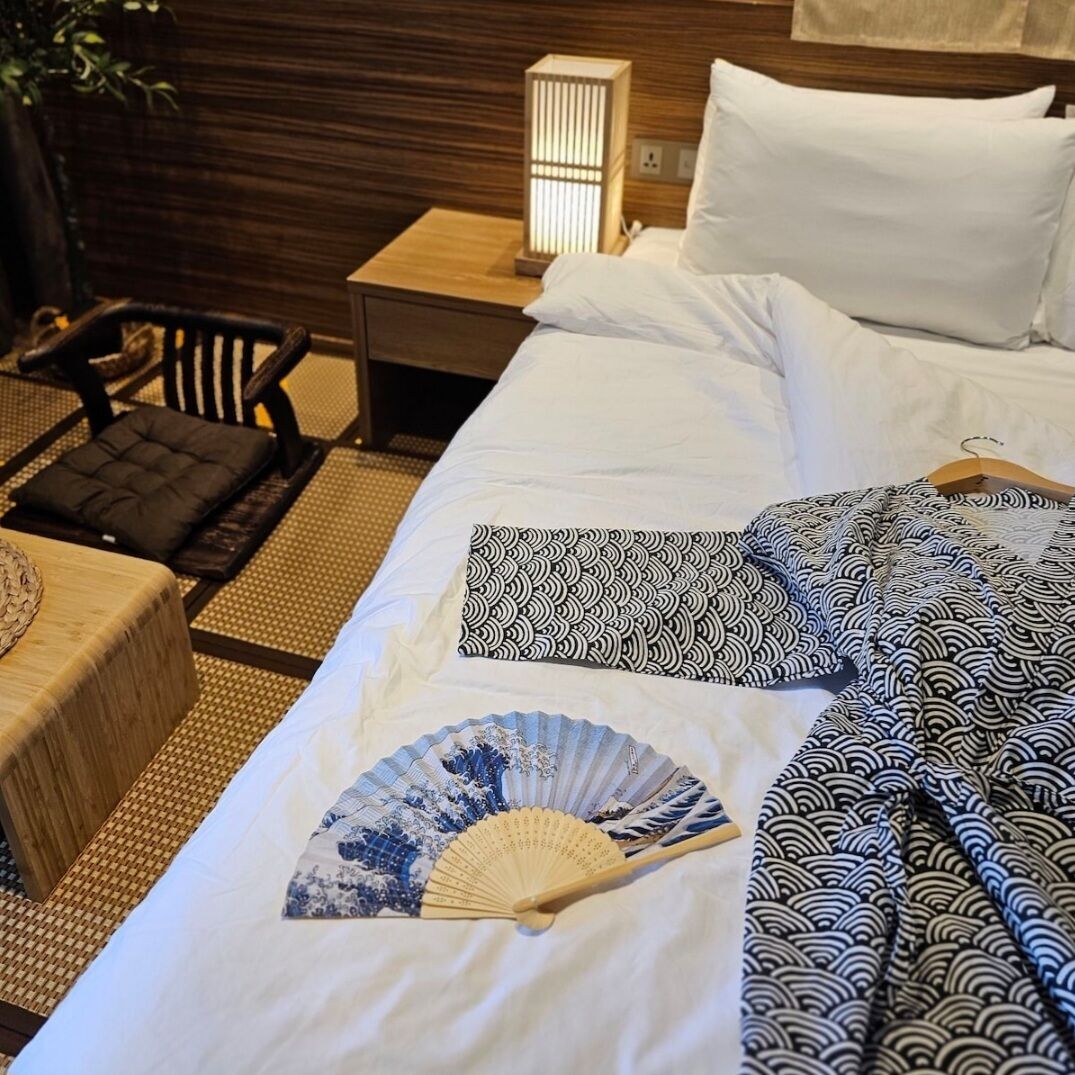 A neatly made bed with white linens, a blue and white fan, and black and white patterned pillows.