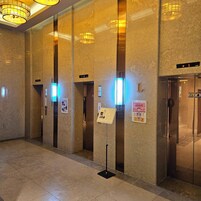 A modern elevator area with marble walls, illuminated by overhead lights, and featuring elevator numbers and directional signs.