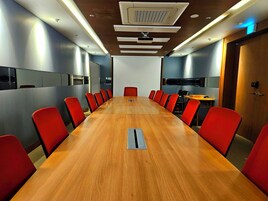 A conference room with a long wooden table, red chairs, and a whiteboard.