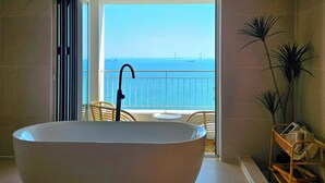 A modern bathroom with a large freestanding bathtub, a view of the sea, and a balcony with wicker furniture. - SainTree Hotel (Incheon)